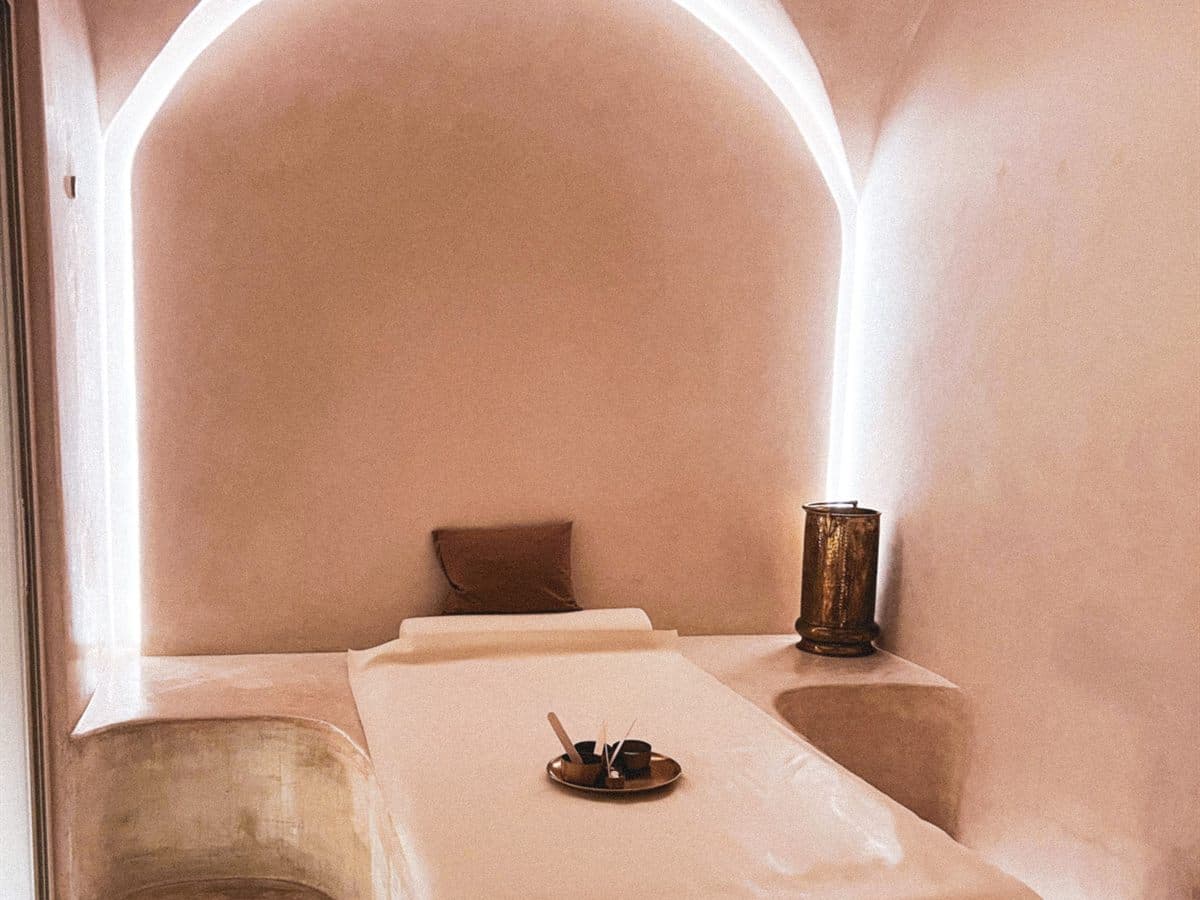 Sala de masaje con bóveda de microcemento en tonos tierra, camilla de obra iluminada con luz indirecta y bandeja con aceites