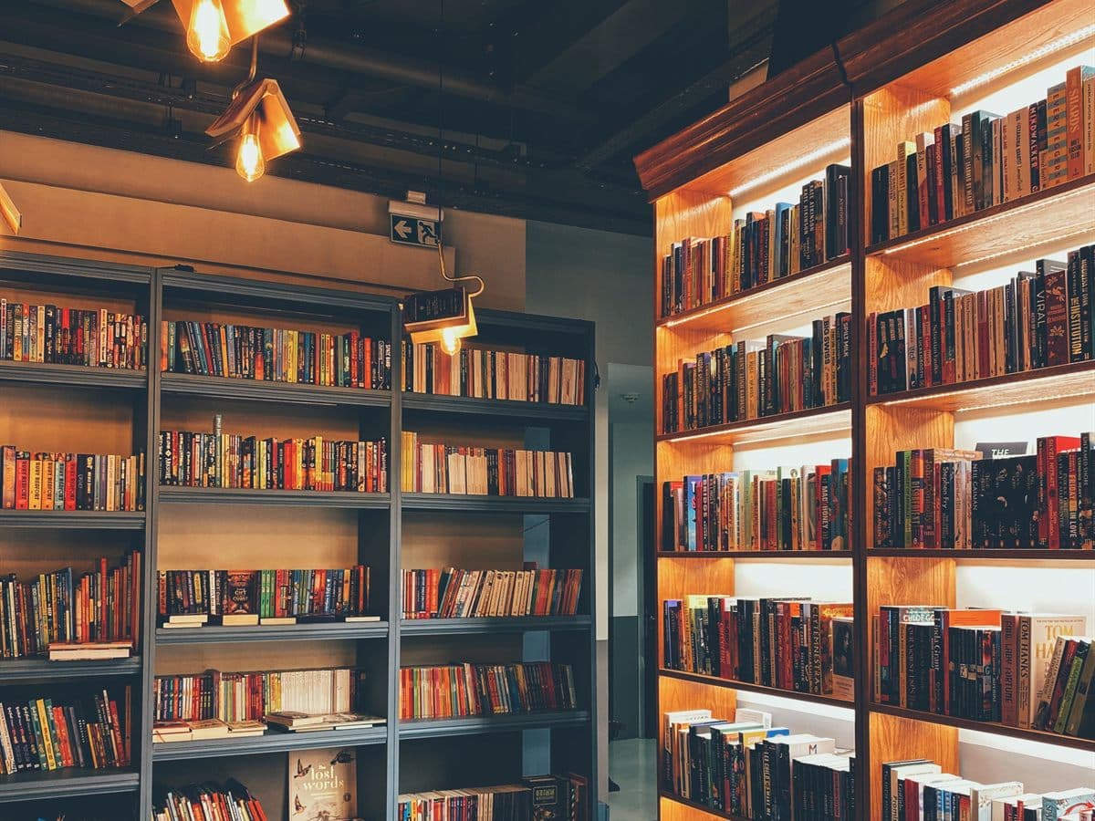 Interior de librería con estanterías de madera iluminadas y libros ordenados del suelo al techo